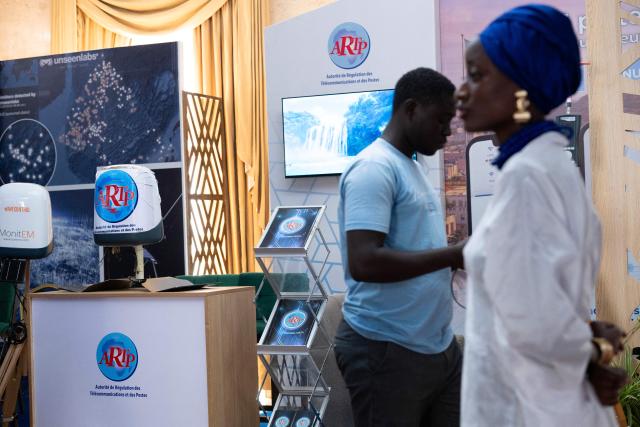 A participant and a hostess stand in front of the ARTP (Telecommunications and Postal Regulatory Authority) booth at the Senegal Space Week 2026 at a Dakar hotel on May 20, 2026. (Photo by SEYLLOU / AFP)