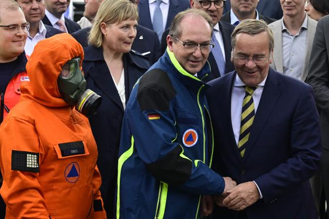 Germany's Interior Minister Alexander Dobrindt (C) and Germany's Defence Minister Boris Pistorius (R) shake hands as first responders stand during a hand over of special vehicles for the civil protection to volunteer emergency personnel in Berlin, on May 20, 2026. On May 20, 2026, six CBRN (Chemical, Biological, Radiological and Nuclear Hazards) command personnel carriers for casualty decontamination (MTW Fü Dekon V) and six federal civil protection ambulances (KTW Typ B) from the Federal Office of Civil Protection and Disaster Assistance (BBK) are handed over to emergency services of the States of Berlin, Brandenburg and Thuringia, as well as a THW personnel carrier to Baden-Württemberg. (Photo by John MACDOUGALL / AFP)