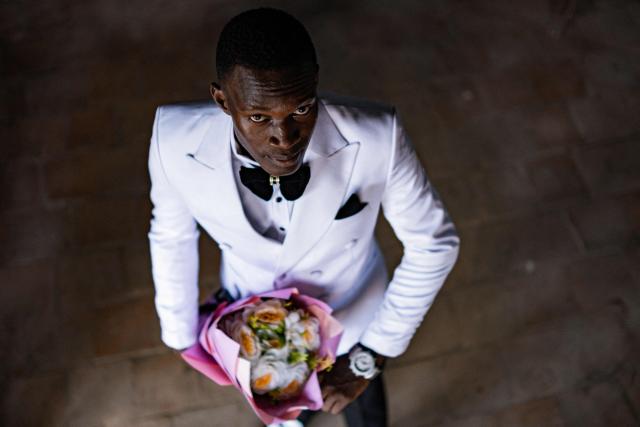 A senior year student at St. Julian High School poses for a picture inside his dormitory after dressing up to attend the school’s prom party themed “A Night in Italy” in Gayaza, on May 19, 2026. Uganda’s high school proms, influenced by global youth and celebrity culture and amplified by social media, have become lavish celebrations blending fashion, creativity and status with local styles of celebration. Mostly seen in elite and urban schools, the events feature themed decor, luxury arrivals and elaborate outfits, with some students previously making headlines for arriving by helicopter before the government banned helicopters and luxury SUV's at school events. Schools balance student expression and modern trends with cultural values and stricter government regulations. (Photo by Badru Katumba / AFP)