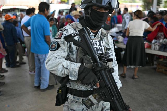 A member of the National Guard is seen as Nahua indigenous women receive humanitaria aid in Alcozacan, a community affected by drug-related violence, in Guerero state, Mexico, on May 19, 2026 (Photo by YURI CORTEZ / AFP)