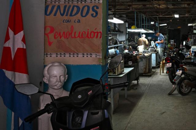 A sign with the slogan "United with the Revolution" is seen at the entrance of a repair workshop in Havana on May 20, 2026. (Photo by YAMIL LAGE / AFP)