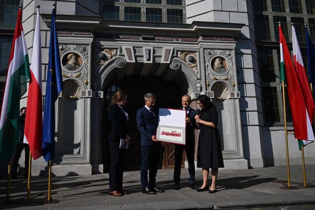 Hungary's Prime Minister Peter Magyar (2nd L), Poland’s Prime Minister Donald Tusk (2nd R) and Mayor of Gdansk Aleksandra Dulkiewicz (R) holp up a signed print with the Solidarnosc logo, during a rally in Gdansk on May 20, 2026. Hungary's new Prime Minister Peter Magyar is on a two-day visit to Poland for his first official trip abroad, hoping to mark his country's re-alignment with the European Union after years of open conflict under his predecessor. (Photo by Sergei GAPON / AFP)