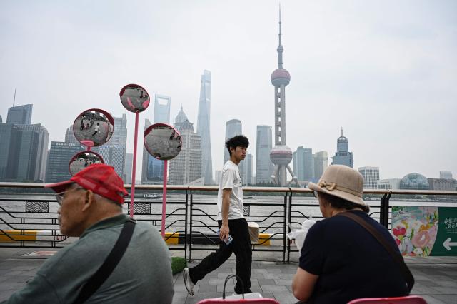 A man walks as two elderly people rest on the North Bund promenade along the Huangpu river in Shanghai on May 21, 2026. (Photo by Jade GAO / AFP)