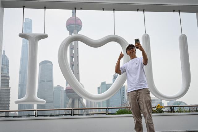 A man takes a selfie in front of an "I love U" installation on the North Bund promenade in Shanghai on May 21, 2026. (Photo by Jade GAO / AFP)