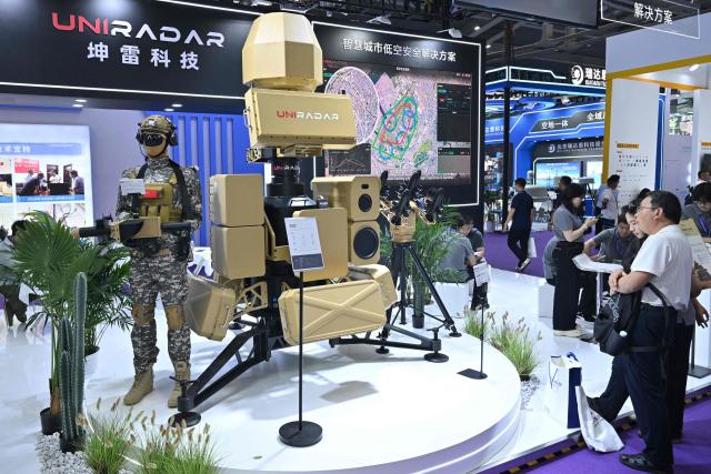 People stand next to an anti-drone system on display at the Uniradar booth during the Drone World Congress (DWC) in Shenzhen on May 21, 2026. (Photo by Hector RETAMAL / AFP)