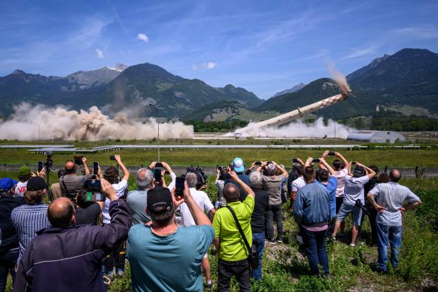 Attendees watch the controlled demolition by explosion of the two 100-metre-high chimneys of a former refinery in Collombey-Muraz, south-western Switzerland on May 21, 2026. Constructed by Eni, the Collombey refinery operated from 1963 to late March 2015, closing after more than 50 years under Tamoil ownership. (Photo by Fabrice COFFRINI / AFP)