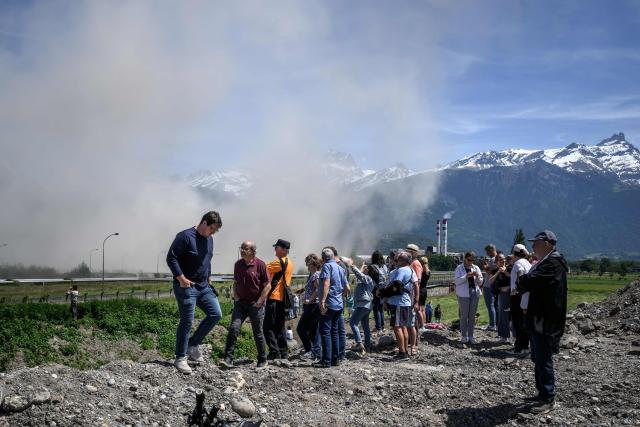 A plume of smoke rises following the controlled demolition by explosion of the two 100-metre-high chimneys of a former refinery in Collombey-Muraz, south-western Switzerland on May 21, 2026. Constructed by Eni, the Collombey refinery operated from 1963 to late March 2015, closing after more than 50 years under Tamoil ownership. (Photo by Fabrice COFFRINI / AFP)