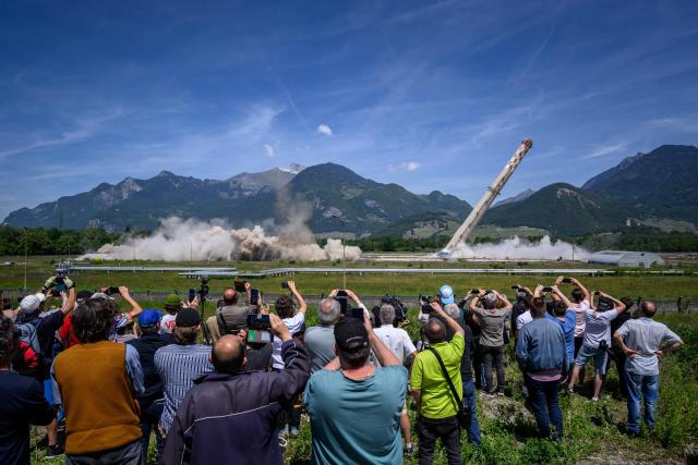 Attendees watch the controlled demolition by explosion of the two 100-metre-high chimneys of a former refinery in Collombey-Muraz, south-western Switzerland on May 21, 2026. Constructed by Eni, the Collombey refinery operated from 1963 to late March 2015, closing after more than 50 years under Tamoil ownership. (Photo by Fabrice COFFRINI / AFP)