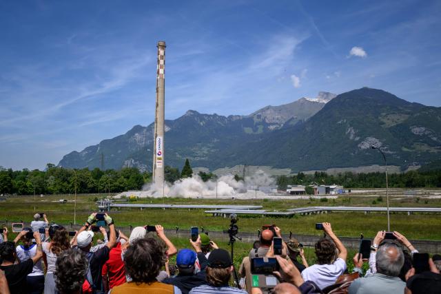 Attendees watch the controlled demolition by explosion of one of the two 100-metre-high chimneys of a former refinery in Collombey-Muraz, southwestern Switzerland on May 21, 2026. Constructed by Eni, the Collombey refinery operated from 1963 to late March 2015, closing after more than 50 years under Tamoil ownership. (Photo by Fabrice COFFRINI / AFP)