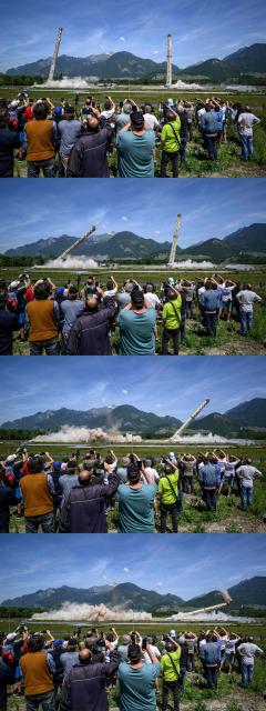 (COMBO) This combination of pictures created on May 21, 2026 shows people watching the controlled demolition by explosion of the two 100-metre-high chimneys of a former refinery in Collombey-Muraz, south-western Switzerland, on May 21, 2026. Constructed by Eni, the Collombey refinery operated from 1963 to late March 2015 was closed after more than 50 years under Tamoil ownership. (Photo by Fabrice COFFRINI / AFP)