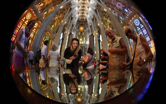 Tourists view the ceiling through a mirror on May 21, 2026 in the nave of the Sagrada Familia basilica in Barcelona. The Sagrada Familia basilica's central tower's cross crowns the world's tallest church at 172.5 meters, a temple conceived by Antoni Gaudi more than 140 years ago. (Photo by Thomas COEX / AFP)