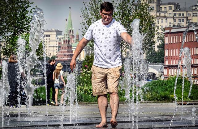 A man refreshes himself in a small fountain, with the Kremlin seen in distance, in downtown Moscow on May 21, 2026, as the temperature raised up to 32 centigrade. (Photo by Alexander NEMENOV / AFP)