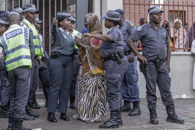 Members of the South African Police Service (SAPS) direct a foreign national to a bus from the Diakonia Centre to the Home Affairs offices in Durban on May 21, 2026. The crowd, made up largely of refugees and foreign nationals had been sheltering at the station for up to two days, seeking police protection amid threats and intimidation. Their presence came against the backdrop of sporadic anti-illegal immigration protests that have unsettled parts of South Africa in recent weeks. (Photo by RAJESH JANTILAL / AFP)