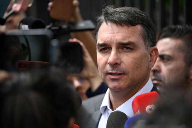 (FILES) Senator Flavio Bolsonaro, son of former Brazilian president Jair Bolsonaro, speaks with journalists after leaving the Federal Police headquarters where his father is being held, in Brasilia, on December 09, 2025. When opinion polls appeared favorable, the scandal broke: Flavio Bolsonaro, the right-wing candidate in Brazil's October presidential election, had dealings with a banker jailed for alleged fraud, threatening to complicate his race against President Lula. The 45-year-old senator was chosen as the political heir by his father, former far-right president Jair Bolsonaro, who was convicted over an attempted coup and barred from running for office. (Photo by Ton MOLINA / AFP)