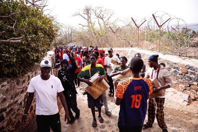 Musicians perform as members of a Martinican delegation walk to the Return Door art installation during a commemoration event marking the abolition of slavery and the 50th anniversary of the historic meeting between Leopold Sedar Senghor and Aime Cesaire on Goree Island, Dakar, on May 21, 2026. (Photo by Lisa Coulaud / AFP)
