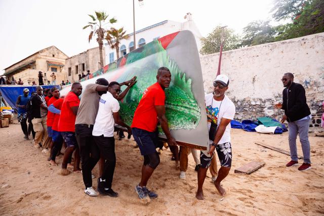 Local officials and members of a Martinican delegation carry a Martinican yole, a wooden sailboat unique to Martinique, during a commemoration event marking the abolition of slavery and the 50th anniversary of the historic meeting between Leopold Sedar Senghor and Aime Cesaire on Goree Island, Dakar, on May 21, 2026. (Photo by Lisa Coulaud / AFP)
