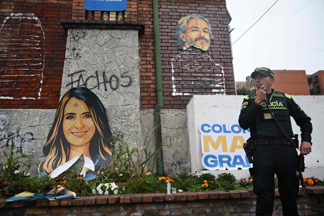 A Colombian police officer stands next to a vandalised banner depicting Colombia's presidential candidate Paloma Valencia and vice-presidential candidate Juan Daniel Oviedo, from the Centro Democratico party, outside the campaign headquarters in Bogota on May 21, 2026. Colombia will hold presidential elections on May 31. (Photo by Raul ARBOLEDA / AFP)