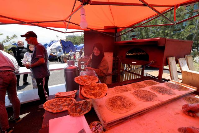 Soubhiye Zeiter, 63, a displaced Lebanese woman who fled her home with her family in Beirut's southern suburbs due to the war between Israel and Hezbollah, distributes mana'eesh, a popular Lebanese flatbread breakfast topped with thyme at a small makeshift bakery in a tented settlement along Beirut's waterfront on May 22, 2026. The government initiative aims to improve living conditions, provide basic services and better manage the growing number of internally displaced people in Beirut following the ongoing crisis. (Photo by Anwar AMRO / AFP)
