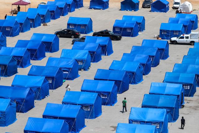 TOPSHOT - Displaced Lebanese walk between blue tents set up by the government for people who fled their homes and villages in Beirut's southern suburbs and southern Lebanon, replacing informal tent settlements in the capital's seafront on May 22, 2026. The government initiative aims to improve living conditions, provide basic services and better manage the growing number of internally displaced people in Beirut following the ongoing crisis. (Photo by Anwar AMRO / AFP)