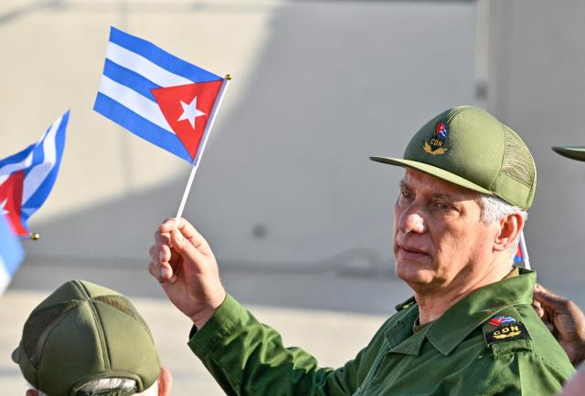 Cuba's President Miguel Diaz-Canel holds a Cuban flag during a rally in support of former Cuban president Raul Castro, 94, who has been indicted by a US court, outside the US Embassy in Havana on May 22, 2026. (Photo by ADALBERTO ROQUE / AFP)