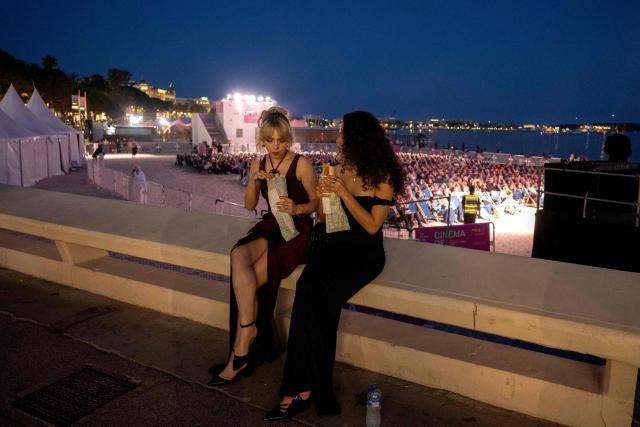 Festival-goers in evening attire eat near the "Cinema de la Plage" on the Boulevard de la Croisette during the 79th edition of the Cannes Film Festival in Cannes, southern France, on May 22, 2026. (Photo by Anna KURTH / AFP)
