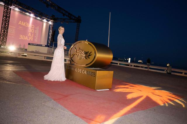 A festival-goer in evening attire poses next to a palm logo on the Boulevard de la Croisette during the 79th edition of the Cannes Film Festival in Cannes, southern France, on May 22, 2026. (Photo by Anna KURTH / AFP)