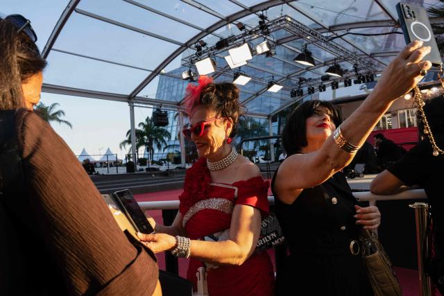 Festival-goers in evening attire take a selfie on the Boulevard de la Croisette during the 79th edition of the Cannes Film Festival in Cannes, southern France, on May 22, 2026. (Photo by Anna KURTH / AFP)