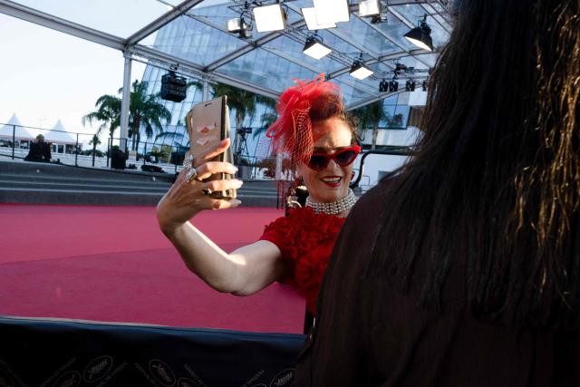 A festival-goer in evening attire takes a selfie on the Boulevard de la Croisette during the 79th edition of the Cannes Film Festival in Cannes, southern France, on May 22, 2026. (Photo by Anna KURTH / AFP)