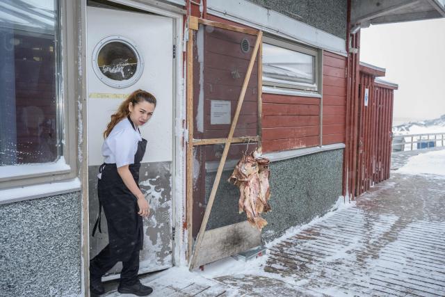 A Thai kitchen hand emerges from the back kitchen into the freezing patio of a restaurant in Ilulissat, Greenland, on March 19, 2026. Around 1,200 Filipinos are settled in Greenland, which has 57,000 inhabitants, making them the largest foreign diaspora in this Danish territory. According to Greenland’s employers’ organisations, 5 to 6% of workers in the Arctic territory are now Asian, drawn by expanding sectors such as tourism. (Photo by Florent VERGNES / AFP)