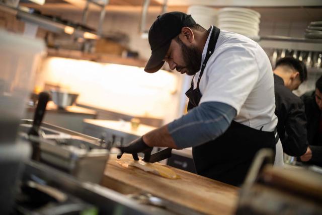A asian cook work on a fish, in the kitchen of a prestigious restaurant in Ilulissat, Greenland, on March 19, 2026. Around 1,200 Filipinos are settled in Greenland, which has 57,000 inhabitants, making them the largest foreign diaspora in this Danish territory. According to Greenland’s employers’ organisations, 5 to 6% of workers in the Arctic territory are now Asian, drawn by expanding sectors such as tourism. (Photo by Florent VERGNES / AFP)