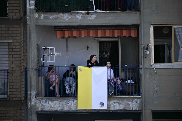People stand on their balcony overlooking Piazza Nicola Calipari to see Pope Leo XIV during a pastoral visit to the community of the 'Land of Fires' on May 23, 2026. The Land of Fires (terra dei fuochi) is an area in the Southern Italian region of Campania were, systematically, since the end of the 80s, toxic wastes have been dumped by organized crime (Camorra) causing waste-related environmental crimes. Acerra and the surrounding territory has higher-than-average cancer rates, linked to the dumping, burning, and burying of toxic waste. (Photo by Filippo MONTEFORTE / AFP)