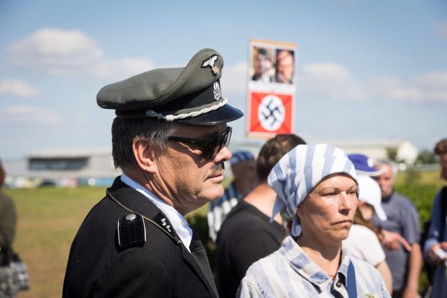 A woman dressed like a concentration camp prisoner and a man in a uniform bearing the runes of Nazi-Germany's paramilitary SS organisation stand along with other protesters to demonstrate against an event organised by the "Union of Expellees within the Christian Social Union party" (UdVA, Union der Vertriebenen, Aussiedler und Deutschen Minderheiten der CSU) to commemorate the flight and expulsion of Sudeten Germans during and after World War II, on May 23, 2026 in Pohorelice, South Moravia, Czech Republic. (Photo by Radek MICA / AFP)