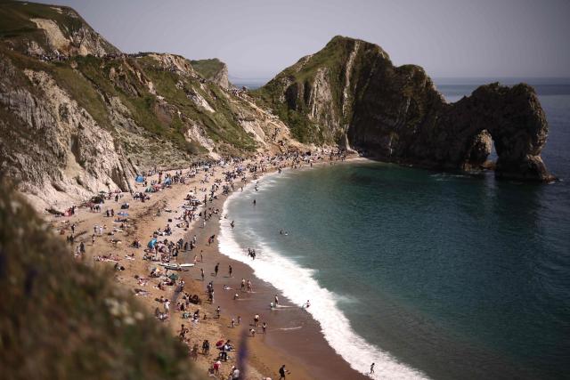 People relax in the sunshine on Durdle Door beach, east of Weymouth on the south coast of England on May 23, 2026, as temperatures are set to rise over the long bank holiday weekend. (Photo by Henry NICHOLLS / AFP)