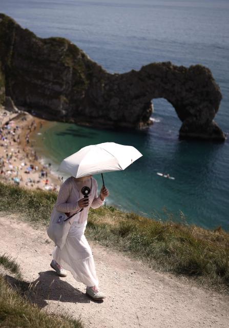 A person uses a parasol on the footpath in the sunshine above Durdle Door beach, east of Weymouth on the south coast of England on May 23, 2026, as temperatures are set to rise over the long bank holiday weekend. (Photo by Henry NICHOLLS / AFP)