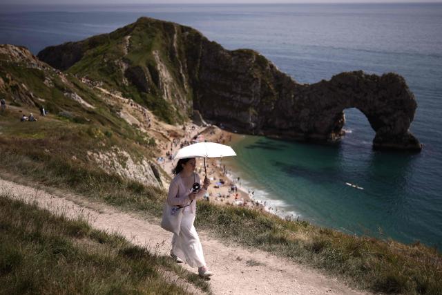 A person uses a parasol on the footpath in the sunshine above Durdle Door beach, east of Weymouth on the south coast of England on May 23, 2026, as temperatures are set to rise over the long bank holiday weekend. (Photo by Henry NICHOLLS / AFP)
