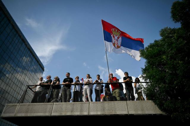 People stand on a balcony as one of them waves a Serbian national flag during an anti-government protest decrying corruption and calling for early elections following the collapse of a railway station canopy in Novi Sad that killed 16 in November 2024, in central Belgrade on May 23, 2026. (Photo by Andrej ISAKOVIC / AFP)