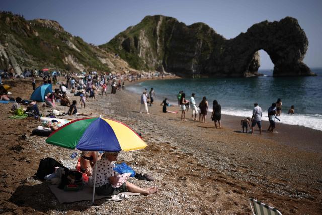 People relax in the sunshine on Durdle Door beach, east of Weymouth on the south coast of England on May 23, 2026, as temperatures are set to rise over the long bank holiday weekend. (Photo by Henry NICHOLLS / AFP)