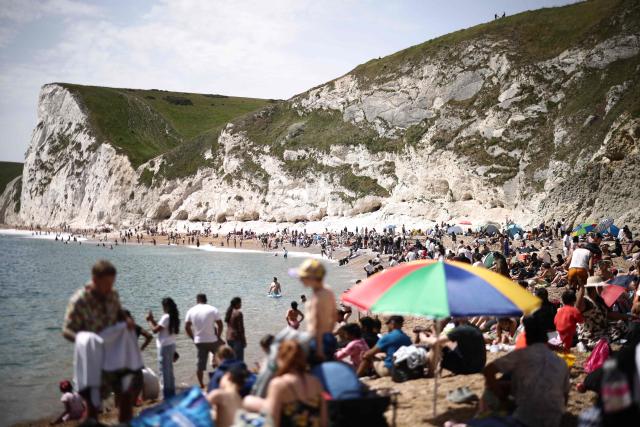 People relax in the sunshine on Durdle Door beach, east of Weymouth on the south coast of England on May 23, 2026, as temperatures are set to rise over the long bank holiday weekend. (Photo by Henry NICHOLLS / AFP)