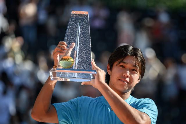 US's Learner Tien celebrates with the winner's trophy after winning the ATP 250 Geneva Open tennis tournament men's singles final match against Argentine's Mariano Navone in Geneva on May 23, 2026. (Photo by Fabrice COFFRINI / AFP)