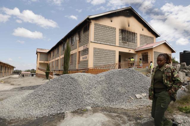TOPSHOT - A Kenyan police officer walks past forensic experts standing near the entrance of a building at Utumishi Girls Academy where a deadly fire took place in Nakuru, north of the capital Nairobi on May 28, 2026. A fire in a girls' dormitory in Kenya on May 28 killed 16 children and hospitalised 79 in the latest deadly blaze to hit a school in the east African country. The fire broke out shortly before 1:00 am local time at Utumishi Girls Academy in Nakuru County, around 120 kilometres (75 miles) north of the capital Nairobi, officials said. (Photo by SIMON MAINA / AFP)