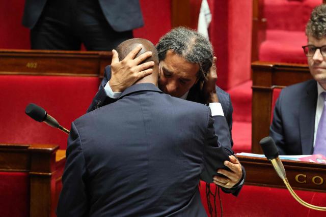 Ecologiste et Social's MP Steevy Gustave (C/R) embraces Libertes, Independants, Outre-Mer et Territoires' MP Max Mathiasin (C/L) as his proposed bill aimed at abolishing the slavery-related laws passed unanimously at The National Assembly, France's lower house parliament, in Paris on May 28, 2026. These laws, known as Code Noir ("Black Code") classified enslaved people as "chattels" that could be acquired by a master in the same way as property, or established penalties for escapeincluding the cutting off of ears, branding with a lily, and even the death penalty. (Photo by Ludovic MARIN / AFP)