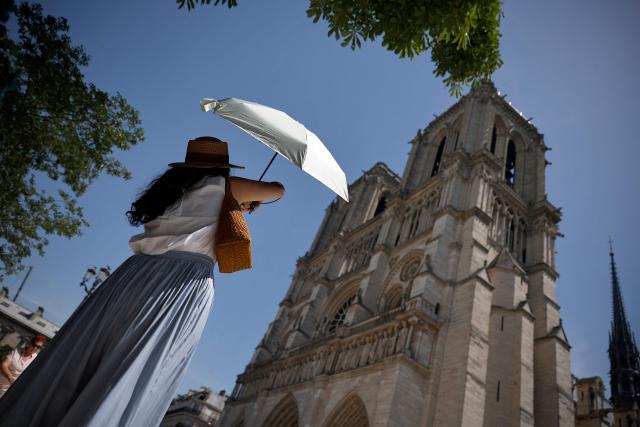 A person protects from the sun under an umbrella in front of Notre-Dame Cathedral in Paris as a record-breaking early heatwave scorches a swathe of western Europe on May 28, 2026. The UK and France have reported their hottest ever May days this week as a "heat dome" brought sizzling temperatures more typical of midsummer to western Europe. UN climate chief Simon Stiell said the heatwave was "a brutal reminder of the spiraling impacts of the climate crisis. "The science is clear that human-induced climate change is making these heatwaves more frequent and extreme," Stiell add in a statement. (Photo by SIMON WOHLFAHRT / AFP)