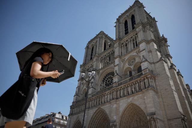 A person protects from the sun under an umbrella in front of Notre-Dame Cathedral in Paris as a record-breaking early heatwave scorches a swathe of western Europe on May 28, 2026. The UK and France have reported their hottest ever May days this week as a "heat dome" brought sizzling temperatures more typical of midsummer to western Europe. UN climate chief Simon Stiell said the heatwave was "a brutal reminder of the spiraling impacts of the climate crisis. "The science is clear that human-induced climate change is making these heatwaves more frequent and extreme," Stiell add in a statement. (Photo by SIMON WOHLFAHRT / AFP)