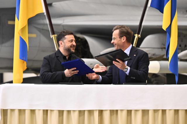 Ukraine's President Volodymyr Zelensky (L) and Swedish Prime Minister Ulf Kristersson exchange documents at a press conference at the F16 air flotilla in Uppsala, Sweden on May 28, 2026. (Photo by Christine Olsson/TT / various sources / AFP) / Sweden OUT