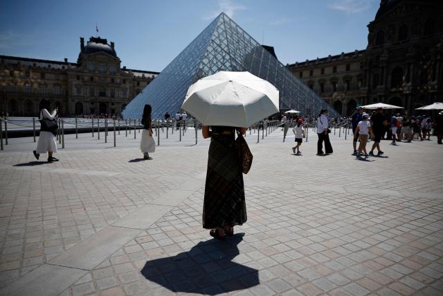 A person protects from the sun under an umbrella in front of the Louvre museum in Paris as a record-breaking early heatwave scorches a swathe of western Europe on May 28, 2026. The UK and France have reported their hottest ever May days this week as a "heat dome" brought sizzling temperatures more typical of midsummer to western Europe. UN climate chief Simon Stiell said the heatwave was "a brutal reminder of the spiraling impacts of the climate crisis. "The science is clear that human-induced climate change is making these heatwaves more frequent and extreme," Stiell add in a statement. (Photo by SIMON WOHLFAHRT / AFP)