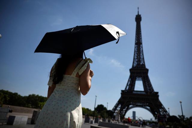 A person protects from the sun under an umbrella while walking toward the Eiffel Tower in Paris as a record-breaking early heatwave scorches a swathe of western Europe on May 28, 2026. The UK and France have reported their hottest ever May days this week as a "heat dome" brought sizzling temperatures more typical of midsummer to western Europe. UN climate chief Simon Stiell said the heatwave was "a brutal reminder of the spiraling impacts of the climate crisis. "The science is clear that human-induced climate change is making these heatwaves more frequent and extreme," Stiell add in a statement. (Photo by SIMON WOHLFAHRT / AFP)