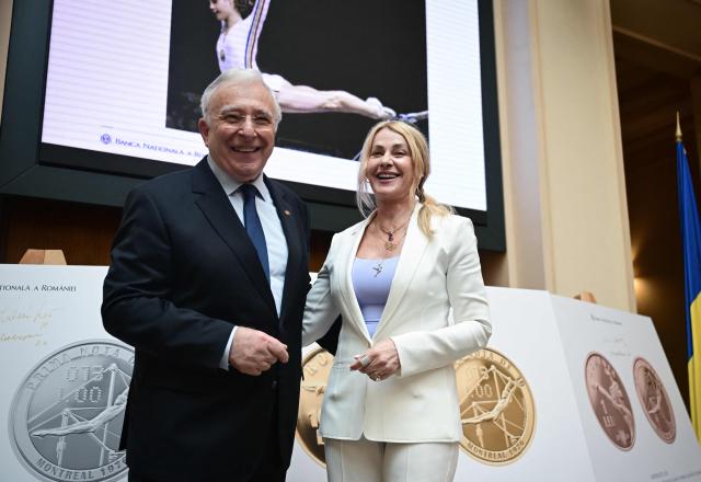 Romanian gymnastics legend Nadia Comaneci (R) and National Bank governor Mugur Isarescu (L) poses next to a prints showing commemorative coins during a ceremony at the National Bank of Romania (BNR) in Bucharest on May 28, 2026. The central bank launched a special numismatic issue—comprising gold, silver, and copper-plated tombac coins—to mark the 50th anniversary of Com?neci achieving the first-ever perfect 10.0 score in Olympic history at the Montreal 1976 Games. The reverse of the coins depicts her iconic uneven bars routine and the historic "1.00" scoreboard display. (Photo by Daniel MIHAILESCU / AFP)