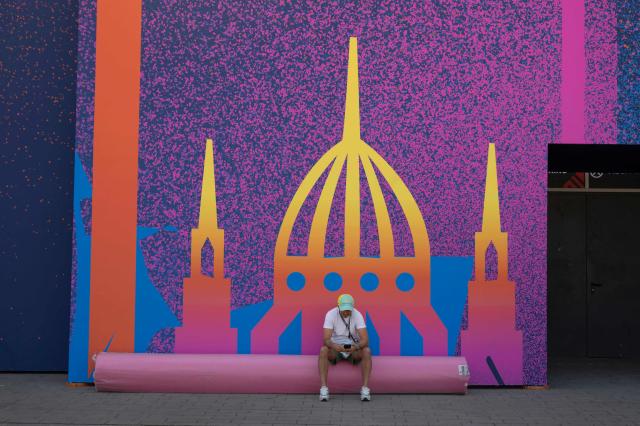 A man sits on a rolled up carpet in front of a silhouette image of Budapest parliament building, at the Puskas Arena on May 28, 2026 ahead of the UEFA Champions League in Budapest on May 28, 2026. The stadium, named after Hungary's most famous footballer Ferenc Puskas, will host the Champions League final between Paris Saint-Germain (PSG) and Arsenal on May 30, 2026. (Photo by Attila KISBENEDEK / AFP)