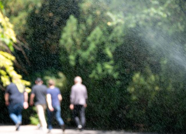People walk past a water sprinkler at the City park (Stadtpark) on a sunny and hot day in Vienna, Austria, on May 28, 2026. Starting in late May, parts of Europe have been affected by heatwaves, breaking records in Spain, the United Kingdom, Germany, France, Ireland. (Photo by Joe Klamar / AFP)
