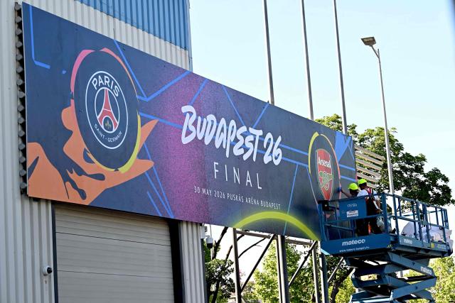 Workers put up a giant UEFA Champions League final poster at the Puskas Arena on May 28, 2026 ahead of the UEFA Champions League in Budapest on May 28, 2026. The stadium, named after Hungary's most famous footballer Ferenc Puskas, will host the Champions League final between Paris Saint-Germain (PSG) and Arsenal on May 30, 2026. (Photo by Attila KISBENEDEK / AFP)